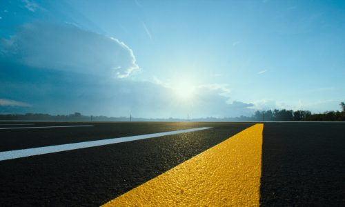 Fresh yellow and white lines on new asphalt under a bright cloudy sky.