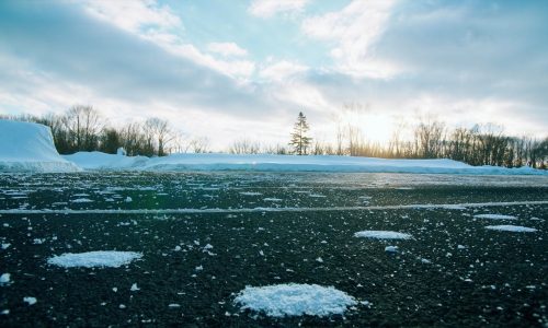 Ice melt pellets spread on cleared asphalt in a plowed parking lot, with snowbanks along the edge.